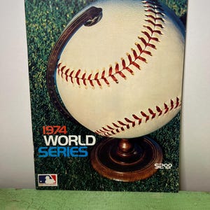 May include: A baseball-themed globe with a white baseball design and red stitching. The base is brown, and the background is green. The text "1974 World Series" is displayed in blue and white. The MLB logo is visible.