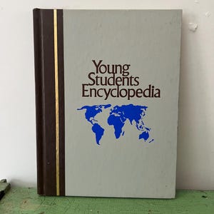 Könnte beinhalten: Ein gebundenes Buch mit dem Titel "Young Students Encyclopedia" mit hellgrauem Einband. Das Buch zeigt eine blaue Weltkarte und einen braunen Buchrücken mit einem goldenen Streifen. Das Buch liegt auf einer grünen Oberfläche.