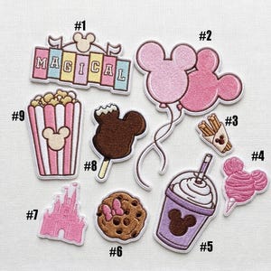 May include: A collection of nine embroidered patches featuring various designs: a sign labeled MAGICAL, two pink mouse-shaped balloons, a container of churros, pink cotton candy, a purple drink, a chocolate chip cookie, a castle, a chocolate treat, and popcorn.