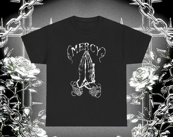 May include: Black t-shirt featuring a white graphic of praying hands with the word "MERCY" above and "Still I Rise" below. The design is in a gothic style. The shirt is a classic crew neck.