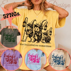 Op de afbeelding: Een geel t-shirt met korte mouwen en een zwarte afbeelding van een kikker, een opossum en een slak met tovenaarshoeden en lantaarns. De tekst "the hullaballoo committee" staat onder de illustratie. Andere kleurvarianten zijn ook zichtbaar.