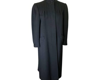 Può includere: Lungo cappotto nero in lana con collo alto e chiusura a bottoni. Il cappotto presenta pieghe sulle spalle e due tasche anteriori. Uno stile classico, adatto ai climi freddi.