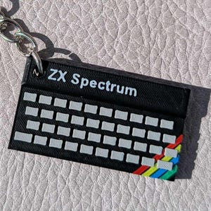 以下が含まれることがあります： 白いキーとカラフルなロゴが付いた、黒いZX Spectrumキーボードキーホルダー。 キーホルダーには、キーやバッグに取り付けるのに最適な、シルバーのキーリングとチェーンが付いています。