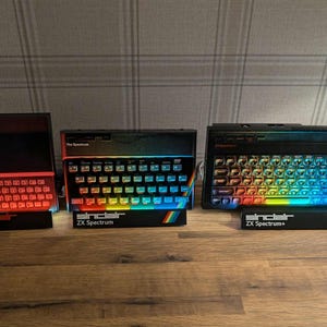 Könnte beinhalten: Drei Vintage Sinclair ZX Spectrum Computer werden gezeigt. Die Tastaturen haben Regenbogenfarben-Tasten. Der Text "Sinclair ZX Spectrum" ist sichtbar. Das ZX81-Modell hat eine rote Beleuchtung.