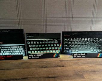 May include: Three black Sinclair computers: ZX81, ZX Spectrum, and ZX Spectrum+. Each has a keyboard and a rainbow stripe. The ZX81 has the text "ZX81" and "Sinclair" in red. The ZX Spectrum has the text "The Spectrum" and "Sinclair ZX Spectrum". The ZX Spectrum+ has the text "ZX Spectrum+" and "Sinclair".