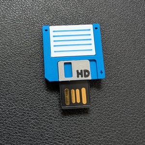 May include: A blue and white 3D-printed USB flash drive shaped like a floppy disk. The drive has the letters "HD" printed on it and a gold-colored USB connector.