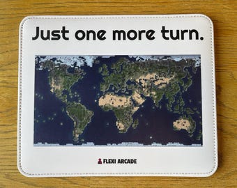 May include: A rectangular white mousepad featuring a pixelated world map graphic in the center. The text Just one more turn. is printed in black at the top, and the text FLEXI ARCADE with a small red icon is printed at the bottom.