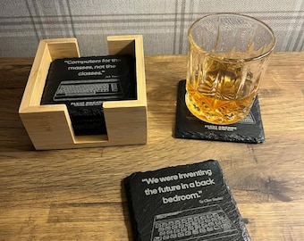 May include: A set of black slate coasters with white text and keyboard graphics. One coaster has the quote "Computers for the masses, not the classes." Another says "We were inventing the future in a back bedroom."