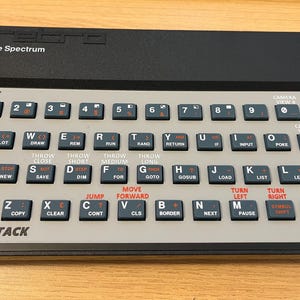 Op de afbeelding: Een zwart en grijs vintage computertoetsenbord met witte toetsen en rode letters. Het toetsenbord heeft een label met de tekst "The Spectrum" en "ANT ATTACK".