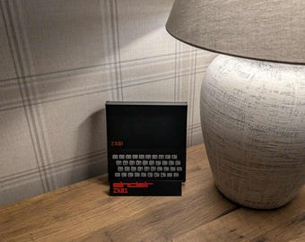 May include: A black Sinclair ZX81 home computer featuring a membrane keyboard with white keys, a black display area, and red text branding on the front panel. The device is rectangular with a compact design and clearly visible model labels.