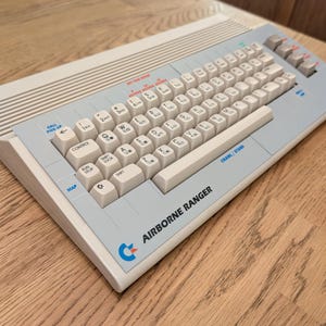 Könnte beinhalten: Ein Vintage Airborne Ranger Computer in Beige und Grau. Die Tastatur hat weiße Tasten mit schwarzer Beschriftung. Das Retro-Design zeigt den Text "AIRBORNE RANGER" und ein Logo auf der Vorderseite.