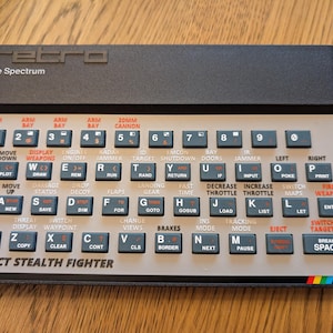 Könnte beinhalten: Eine Retro-Computer-Tastatur mit dem Text "retro" und "The Spectrum" oben. Die Tastatur hat zahlreiche beschriftete Tasten, darunter "Project Stealth Fighter" unten und einen Regenbogenstreifen unten rechts.