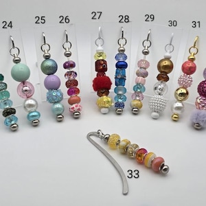 May include: A collection of beaded bookmarks and earrings. The earrings are displayed on clear plastic cards. The beads are in various colors, including blue, green, pink, purple, gold, and red. The bookmark has a silver-colored metal base.