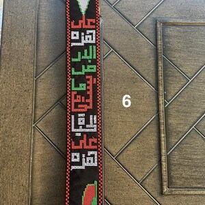 May include: A black fabric strap with a woven design featuring the Palestinian flag colors of red, green, white, and black. The strap has Arabic text woven into the design.