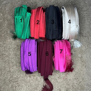 May include: Seven different colors of ribbon with tassels. The colors are green, red, black, silver, purple, burgundy, and pink.