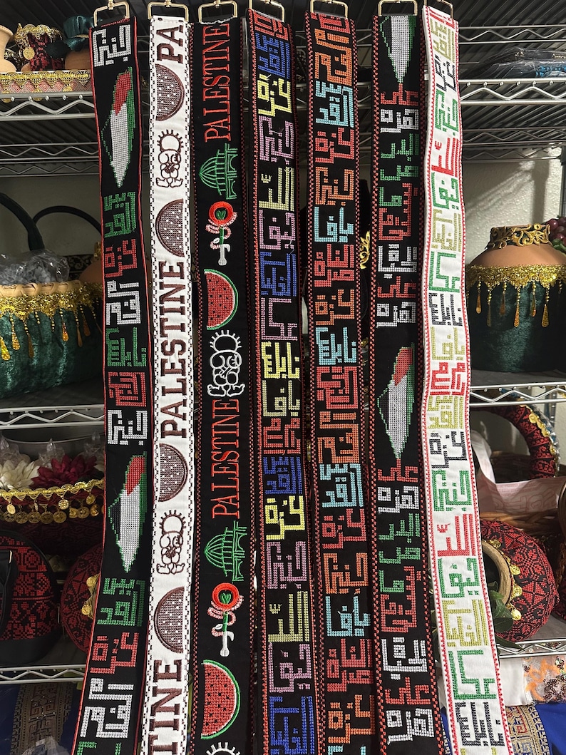 May include: Six colorful woven belts with the word "Palestine" written in Arabic script. The belts are decorated with various symbols, including a watermelon, a mosque, and a key.