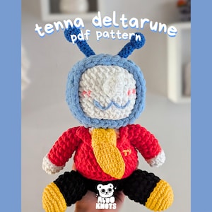 Puede incluir: Muñeca de ganchillo hecha a mano con cabeza y antenas azules, cara blanca y chaqueta roja. La muñeca tiene una corbata amarilla y pantalones negros con detalles amarillos. El texto "tenna deltarune pdf pattern" es visible.