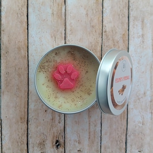 May include: A small, round tin candle with a pink paw print on top. The candle is labeled "Feline's Fireball" and has a cinnamon scent.