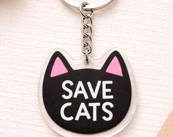 May include: A clear acrylic keychain with a cat face design. The cat's face is black with pink inner ears. The words "SAVE CATS" are in white block letters. The keychain has a silver metal ring and chain.
