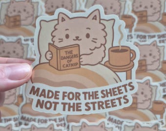May include: A sticker depicting a cartoon cat in bed reading a book titled "The Dangers of Catnip", with a coffee mug on a side table. The sticker has the text "Made for the Sheets Not the Streets".