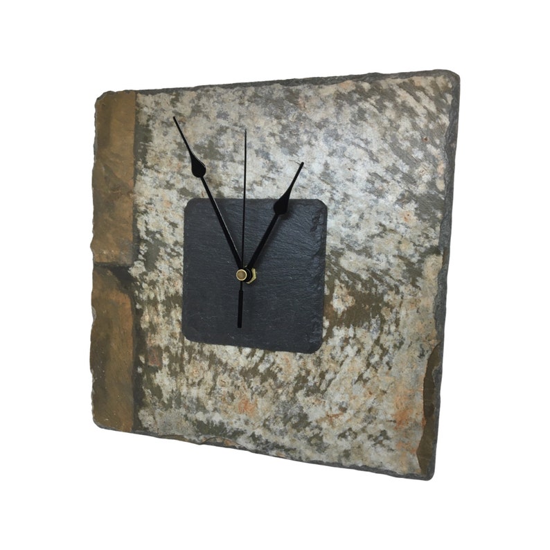 May include: Square slate clock with a natural stone appearance. The clock face is a dark gray square with black clock hands and a gold-colored center. The clock's stone has shades of gray, brown, and tan.