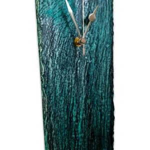 May include: A teal green slate clock with silver hands and a gold knob. The clock has a rough, textured surface.