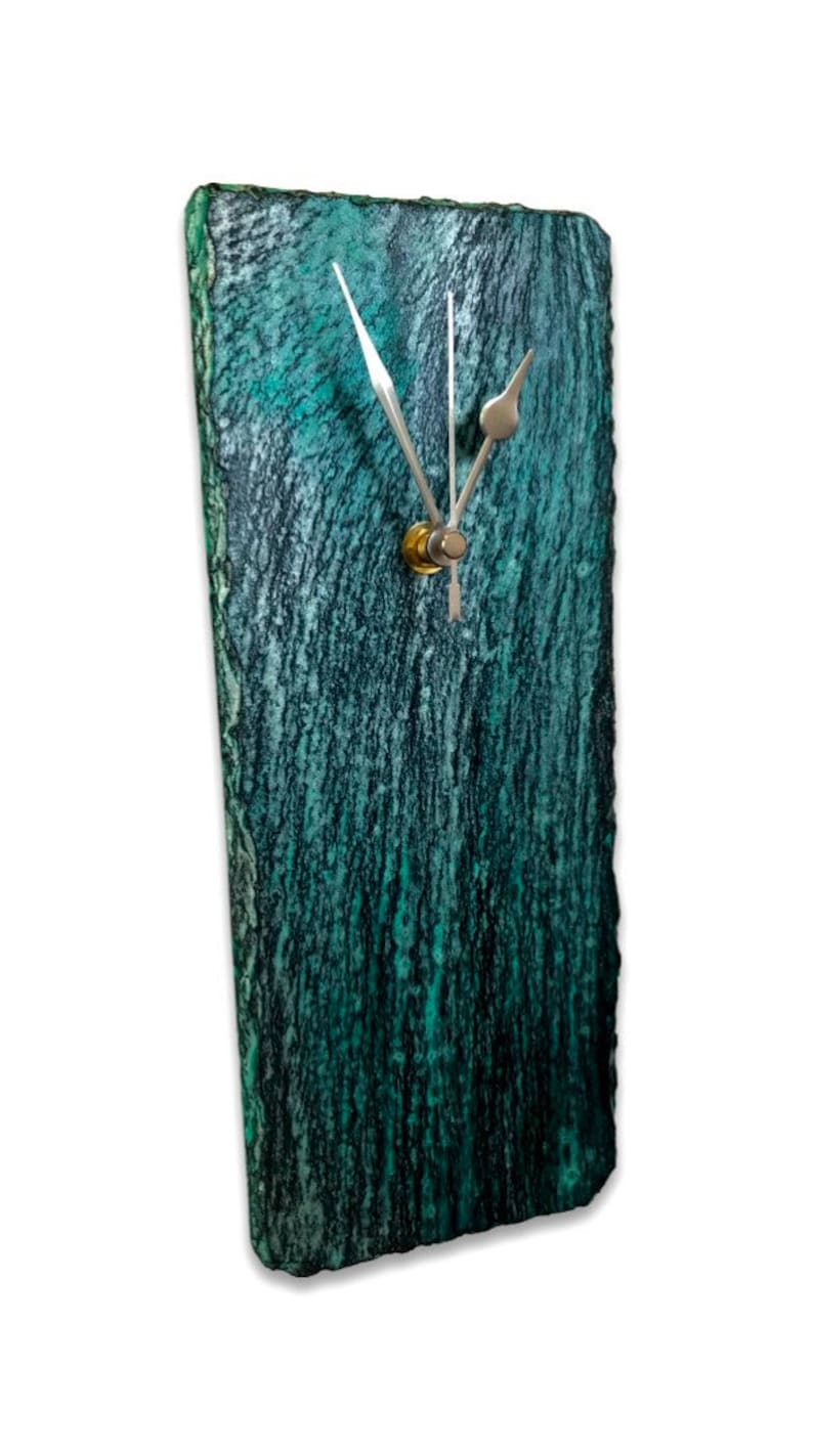 May include: A teal green slate clock with silver hands and a gold knob. The clock has a rough, textured surface.