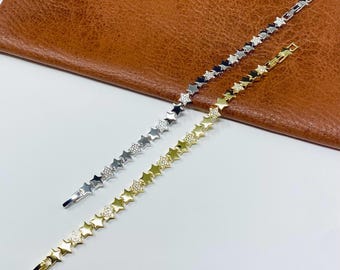 May include: Two star-shaped bracelets. One is silver with clear stones, the other is gold with clear stones. The bracelets are on a white surface with a brown leather background.