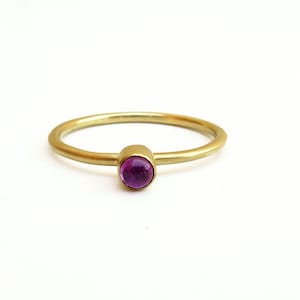 May include: A simple gold band ring with a small, round, cabochon-cut purple gemstone.