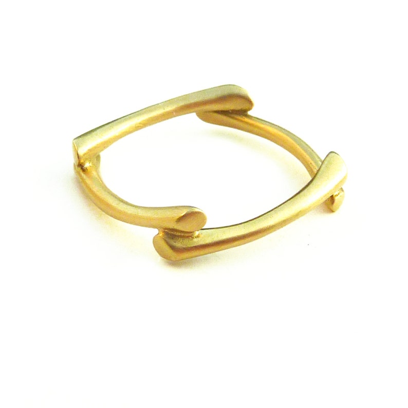 May include: A gold ring with a unique, abstract design. The ring is made of two pieces of metal that are intertwined.
