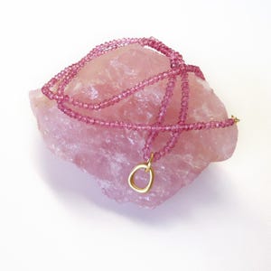 May include: A pink gemstone necklace with a gold pendant. The necklace is made of small, round beads and is draped over a large, pink crystal.