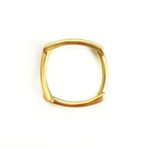 May include: A gold-colored metal ring with a square shape. The ring is made of four pieces of metal that are joined together.
