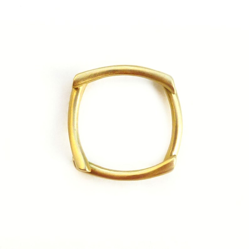 May include: A gold-colored metal ring with a square shape. The ring is made of four pieces of metal that are joined together.
