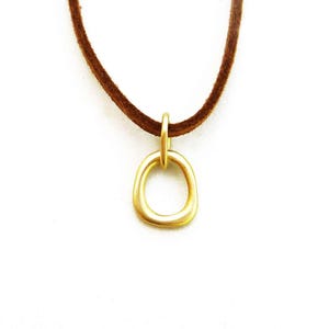 May include: A gold-colored pendant necklace with a simple, rounded circle design. The necklace is made of suede leather and has a brown color.