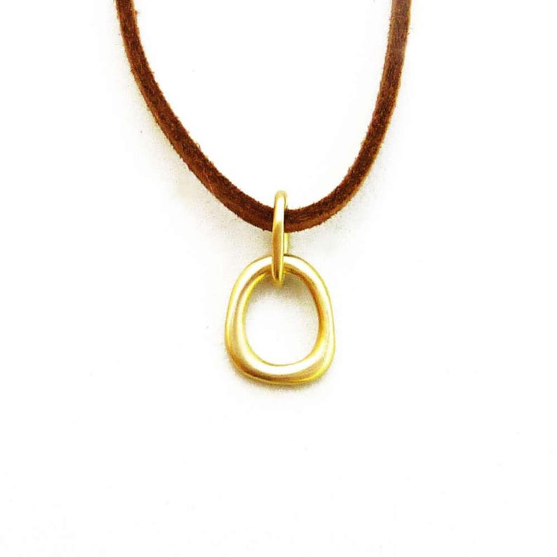 May include: A gold-colored pendant necklace with a simple, rounded circle design. The necklace is made of suede leather and has a brown color.