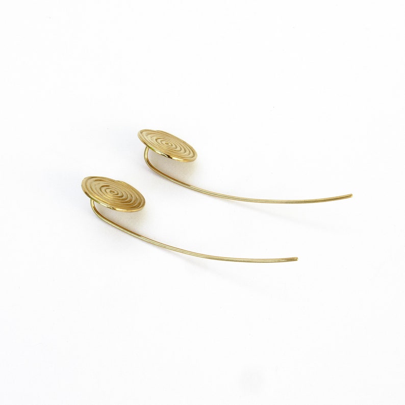 May include: A pair of gold earrings with a spiral design. The earrings are long and thin, with a small, round disc at the top.