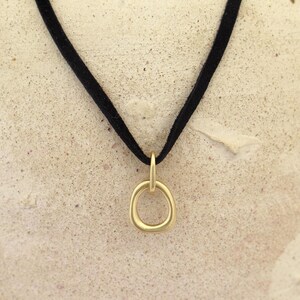May include: A gold pendant necklace with a simple, rounded circle design. The necklace is on a black suede cord.