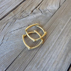 May include: Two gold square hoop earrings, stacked on top of each other, on a wooden surface.