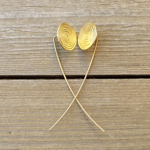 May include: A pair of gold earrings with a circular design. The earrings are suspended from thin, gold wires.