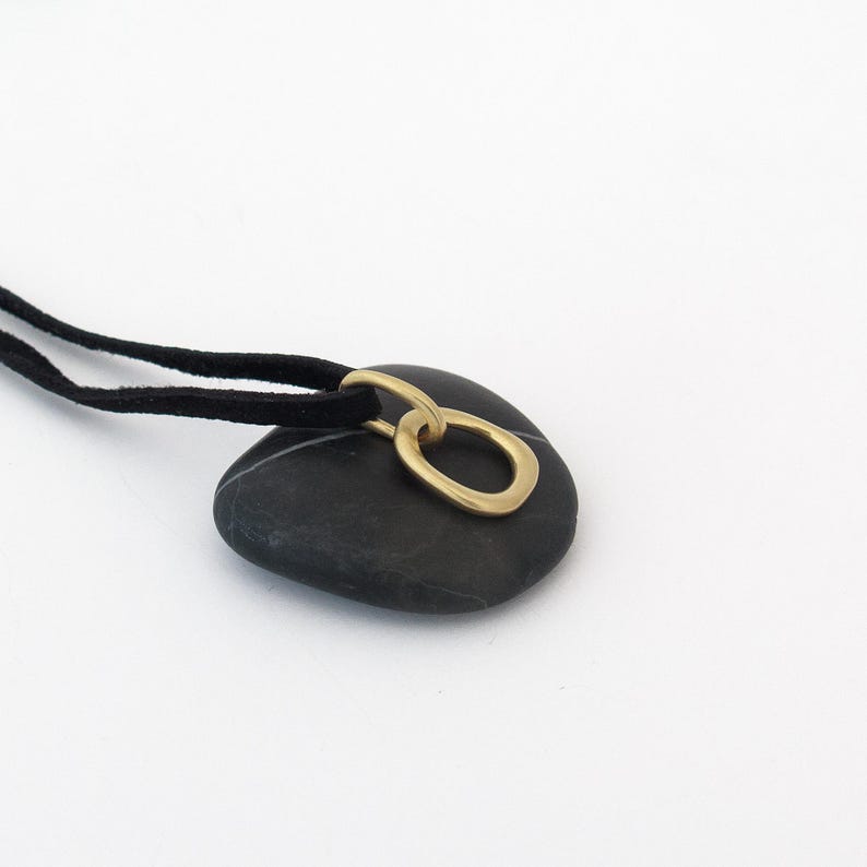 May include: A black stone pendant necklace with a gold oval ring charm. The necklace is made with a black suede cord.
