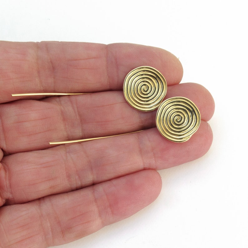 May include: A pair of gold-toned earrings with a spiral design. The earrings are on a white background.