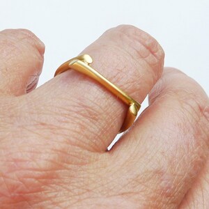 May include: A gold ring with a unique, abstract design. The ring is open and appears to be made of a single piece of metal.