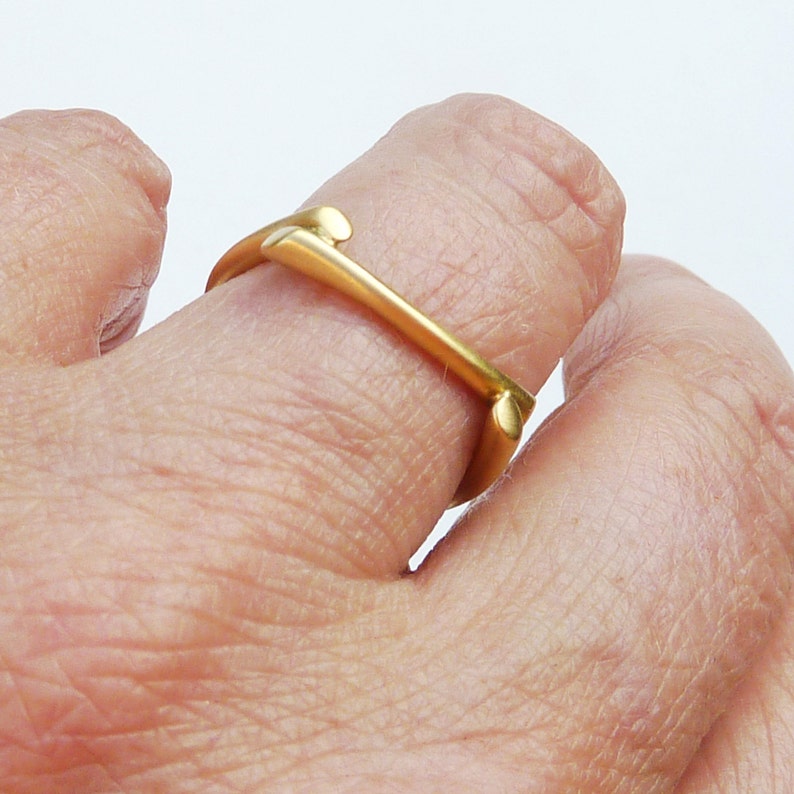 May include: A gold ring with a unique, abstract design. The ring is open and appears to be made of a single piece of metal.