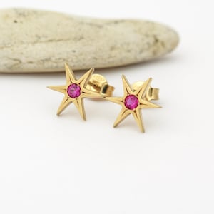 May include: A pair of gold star-shaped earrings with a pink gemstone in the center of each star.