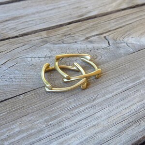 May include: Two gold-colored metal rings, stacked on top of each other, on a wooden surface.