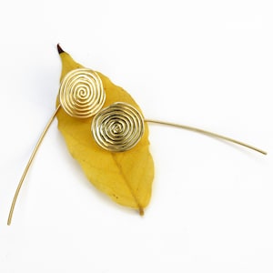 May include: A pair of gold-toned earrings with a spiral design. The earrings are on a yellow leaf.