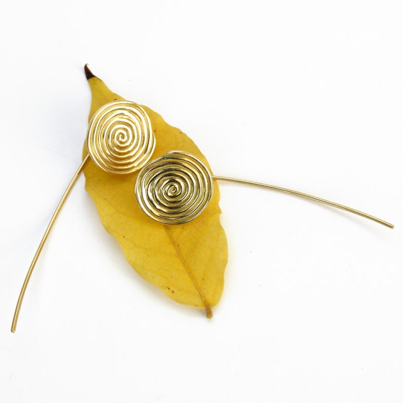May include: A pair of gold-toned earrings with a spiral design. The earrings are on a yellow leaf.