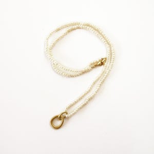 May include: A delicate gold necklace with a simple circle pendant and a double strand of white pearls.