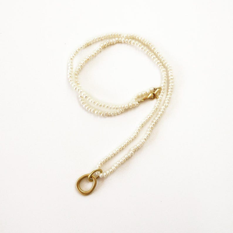 May include: A delicate gold necklace with a simple circle pendant and a double strand of white pearls.