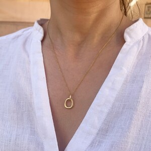 May include: A gold chain necklace with a simple, organic-shaped pendant. The pendant is a circle with a slightly irregular shape.
